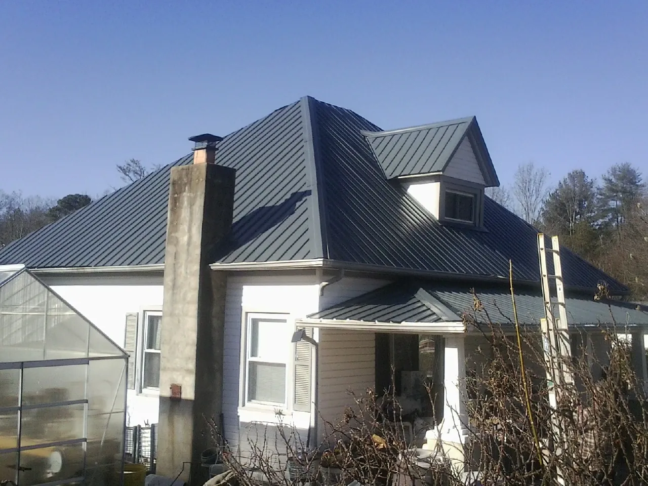 Dark blue standing seam metal roof on a white farmhouse with dormer — Slate & Tile Roof Repair by Roofing Brothers in Coal Township
