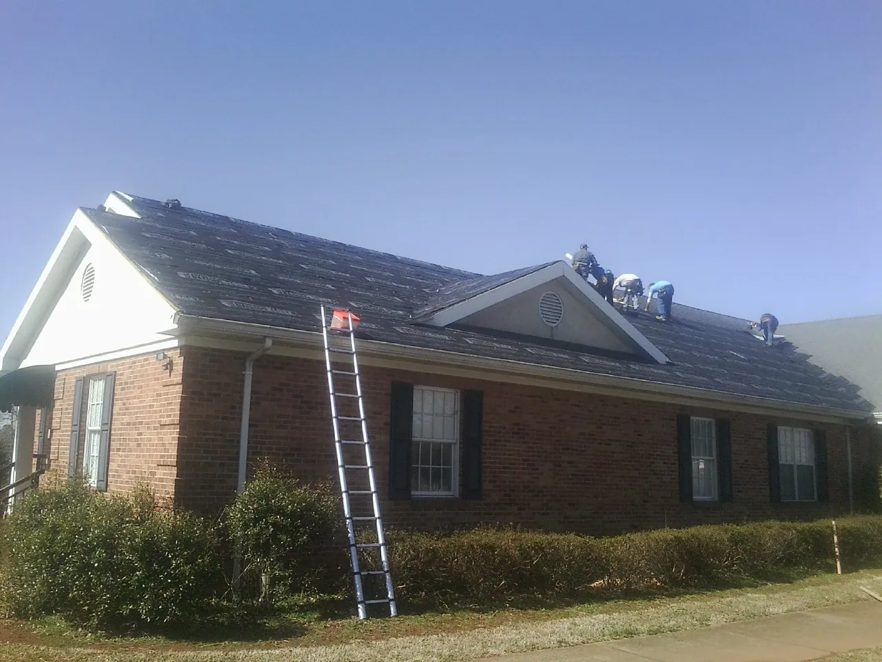 Crew tearing shingles off a brick ranch roof with a ladder set — Metal Roof Repair work by our crew in Coal Township