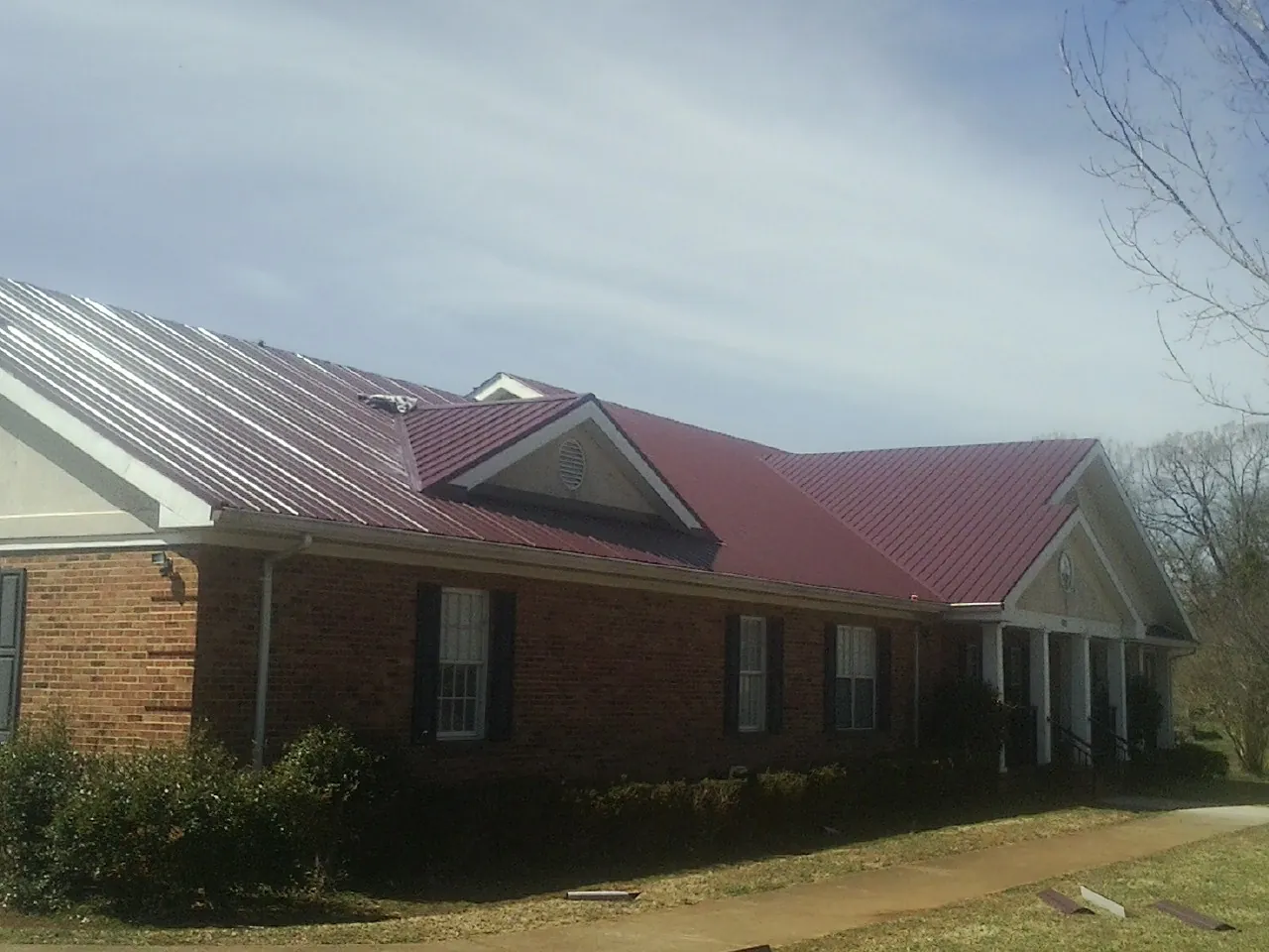 Red metal roof with gabled entries on a long brick building, from a Hail Damage Roof Repair job in Coal Township