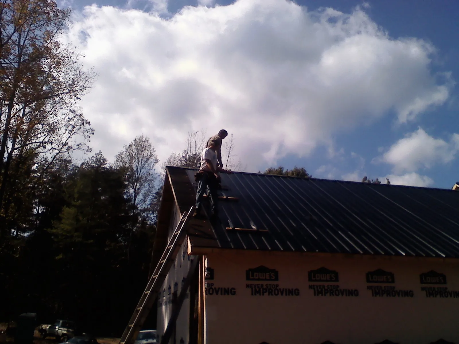Roofer fastening dark metal panels high against a cloudy sky, from a Roof Inspection job in Coal Township