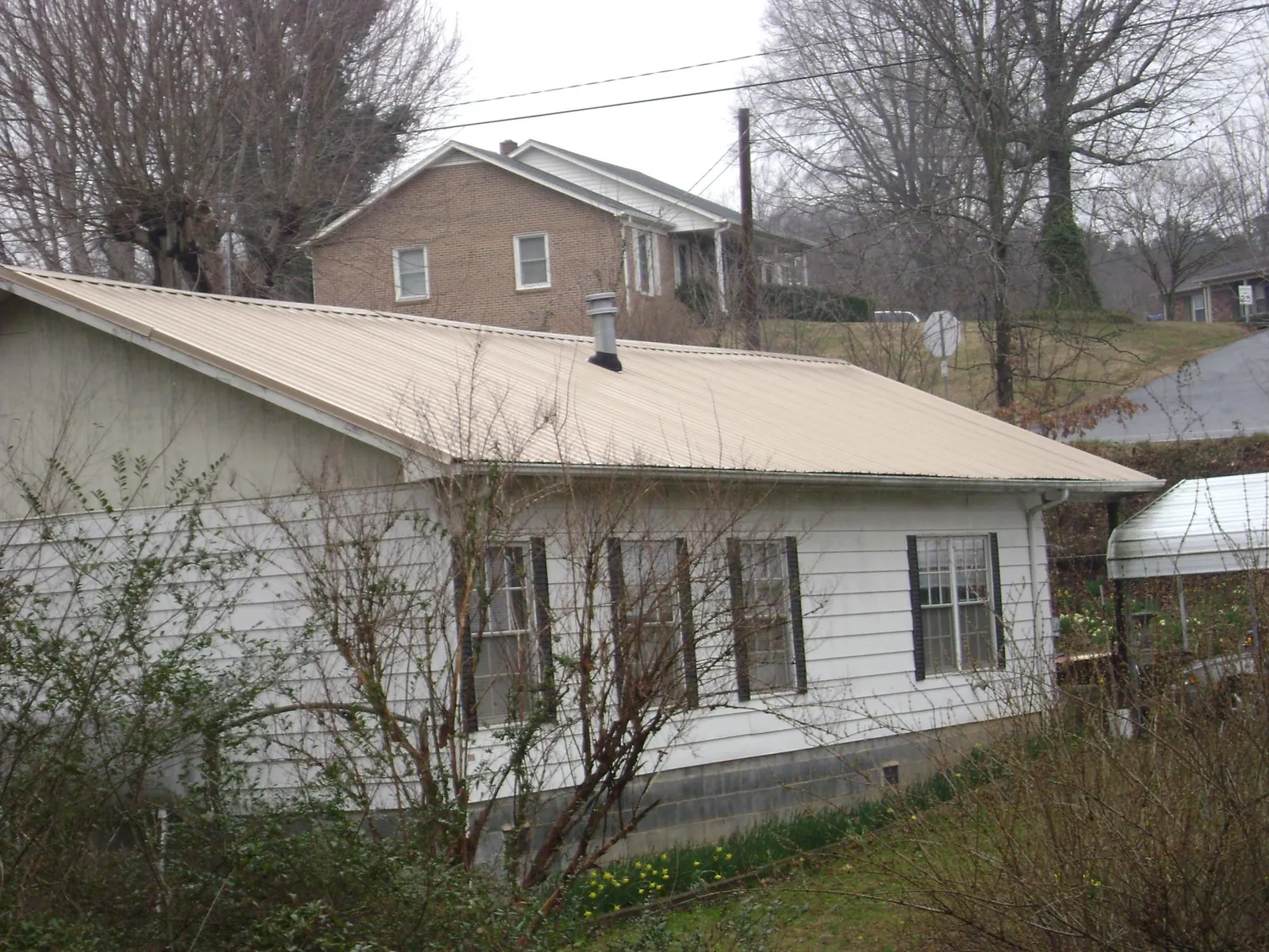 Tan metal roof on a white sided house set into a hillside — Commercial Roofing by Roofing Brothers in Coal Township